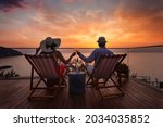 A romantic couple sitting in lounge chairs on summer vacation enjoys the sunset over the mediterranean sea with a glass of wine