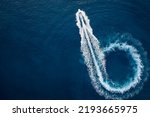 Aerial top view of a motor powerboat forming a circle of waves and bubbles with its engines over the blue sea