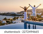 A happy family on summer holidays stands by the swimming pool and enjoys the beautiful sunset behind the mediterranean sea in Greece