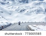 Austria, Tyrol, High Alpine road. Snowy scenery. Couple traveling by motorcycle, moving on speed by road curve of Grossglockner Hochalpenstrasse at snowy Alps mountains background. Sunny May day.