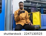 An African-American courier rides in a subway car and watches a TV series on his phone while he goes to pick up an order