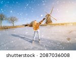 Girl having fun on ice in typical dutch landscape with windmill. Woman ice skating on rink outdoors in sunny snowy day. Outdoor activity on frozen canal in winter Christmas Eve