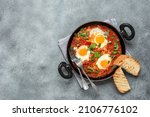 Small photo of Shakshuka in a frying pan on a black stone rustic background. Poached eggs in a spicy tomato pepper sauce. Traditional Jewish scrambled eggs. Top view, flat lay. Textured object, selective focus.