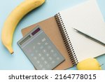 Paper notebook with calculator, pen, bottle of water and fruits on blue background. Healthy eating concept - calculate daily nutrition intake. Top view.
