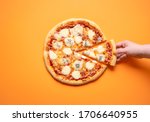 Quattro formaggi pizza and a woman hand taking one pizza slice, on an orange seamless background. Flat lay with 4 cheese pizza. Delicious Italian food.