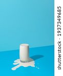 Small photo of Glass of milk overflowing on a blue background in bright light. Spilled milk puddle and glass of milk on a colored table.