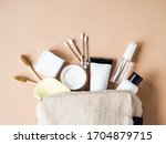Small photo of Travel cosmetic bag with the necessary means to care for women's skin. Cosmetics, dry shampoo, cotton buds, toothbrushes next a cosmetic bag on a beige background. top view