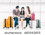 Group of young Asian travelers using smartphone checking flight or online check-in at airport together, with luggage. Travel abroad, summer holiday trip, or mobile phone application technology concept