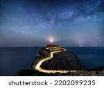 Milky way rising over an illuminated road with light trails at the Far de Formentor lighthouse on the island of Mallorca, Spain