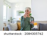 Small photo of Senior woman takes pill with glass of water in hand. Stressed female drinking sedated antidepressant meds. Woman feels depressed, taking drugs. Medicines at work