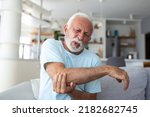 Small photo of Senior man with arm pain.Old male massaging painful hand indoors. Old man hand holding his elbow suffering from elbow pain. Senior man suffering from pain in hand at home. Old age, health
