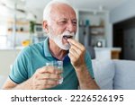 Small photo of Senior man takes pill with glass of water in hand. Stressed mature man drinking sedated antidepressant meds. Man feels depressed, taking drugs. Medicines at work