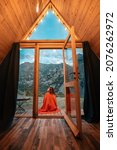 Small photo of Alone woman on the porch of a small wooden house in the mountains.. The concept of glamping and idyllic holidays