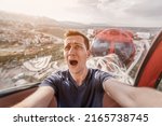 A guy with acrophobia or fear of heights screams with funny emotions on his face from the view from a high Ferris wheel in an amusement park