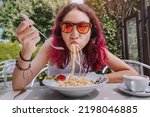 Small photo of The girl is in a funny hurry and eats Italian pasta in a cafe. The concept of good manners and rules of etiquette on the first date