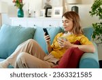 Woman using smartphone while drinking coffee at her home in the morning