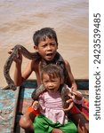Small photo of Siem Reap,Camboda,July 6, 2019-A young boy and girl eke out a living for their family by getting tips from tourists along with their pet python on the Tonle Sap lake near Siem Reap,Cambodia