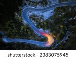 A drone view of a winding mountain road, illuminated by streaks of light from passing cars. Long exposure, dynamics and atmosphere.  