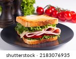 Close-up of two toasted sandwiches with fresh ham, cheese and vegetables on background. Club sandwich and take-away concept. Fast food. 