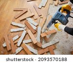 Small photo of Parquet in wood glued to the slab, removed with an electric demolition hammer by a craftsman in workwear, in the apartment under renovation. In the foreground, the removed parquet slats