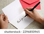 A woman hands writing a Thank You note on a greeting card with red envelope
