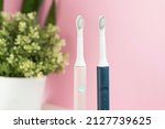 Small photo of New modern ultrasonic toothbrushes. Dental care supplies with green leaves on pink pastel background. Oral hygiene, gum health, healthy teeth. Dental products Ultrasonic vibration toothbrush.