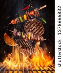 Small photo of Tasty beef steaks and skewers flying above cast iron grate with fire flames. Freeze motion barbecue concept.