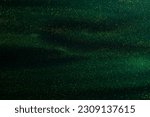 Small photo of Glittering flows of gold particles in green fluid. Various stains and overflows of gold particles in liquid. Abstract shimmering background with flows of golden glitters dust.