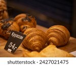 Small photo of Two croissants lie on a shelf in a bakery behind them, two more sprinkled with chocolate. The inscription "croissant 54". this delicacy costs 54 rubles