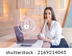 Small photo of Attractive businesswoman in white shirt at workplace working with laptop to defend customer cyber security. Concept of clients information protection. Padlock hologram over office background.