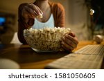 Close-up of unrecognizable woman eating popcorn while using computer at night at home. 