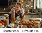 Smiling woman enjoying in taste of healthy food while making avocado bruschetta in the kitchen. 