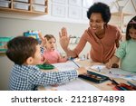 Happy African American teacher and small boy giving high-five during art class at kindergarten. 