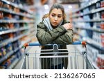 Small photo of Young woman buying in supermarket and feeling worried about increase in food prices.