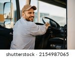 Small photo of Happy professional driver entering in truck cabin and looking at camera.