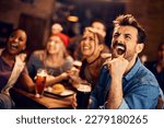 Young man screaming while watching sports game with his friends in a bar.