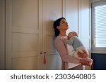 Small photo of Distraught mother thinking of something while her baby is napping in her arms. Copy space.