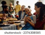 Happy African American girl and her mother laughing while gathering with their extended family on Thanksgiving at home.