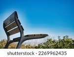 Beautiful wooden and metal bench on a hill in a park with blue sky in the background.
