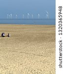 Small photo of Great Yarmouth Norfolk England August. Wind farm electricity generators in the North Sea. Beach to front with two people thereon. Blue sky.