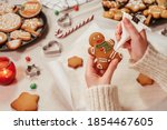 Woman is decorating a traditional gingerbread man. Christmas and New Year holidays mood. Close up view of home kitchen table in preparation