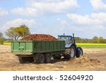 a blue tractor with a green trailer full of freshly harvested carrots leaving the field with a beautiful landscape and blue sky background