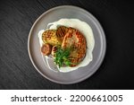 Chicken steak with vegetables in a ceramic plate on a dark textured background. Restaurant menu Isolated on black