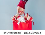 Cropped image of female hand with red polished nails holding shopping bag full of christmas gift boxes. Holiday sale concept. 