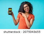 Small photo of Dark skinned girl with perfect smile showing sincere excitement about victory at bookmaker's website. Lady being happy winning bet in online sport gambling application on mobile phone.