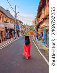 Small photo of Kochi, Kerala, India 30.12.2023 - woman in red skirt with sun umbrella walking in the middle of the street in the colonial heritage district of Fort Kochi