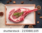 Small photo of Fresh Tomahawk beef steak with rosemary on wooden plate, Tomahawk beef steak on black wooden background.
