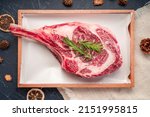 Small photo of Fresh Tomahawk beef steak with rosemary on wooden plate, Tomahawk beef steak on black wooden background.