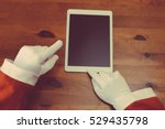 Joyful Christmas online shopping. Closeup on Santa Claus working using mobile tablet computer on wooden table background. Social network, electronic commerce, banking, logistic operations, resolution