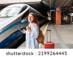 Young redhhead woman waiting train with backpack and using smart phone. Railroad transport concept, Traveler.Woman with suitcase walking at railroad station platform. Travel to vacation by train